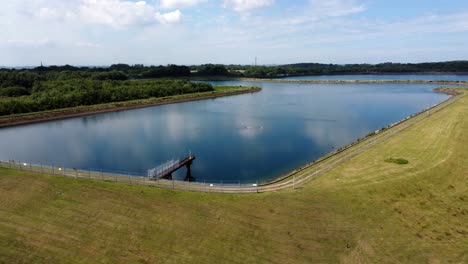 Vista-Aérea-Dolly-A-Través-Del-Depósito-De-Suministro-De-Agua-Reflejos-Del-Cielo-Azul-En-El-Lago-Rural