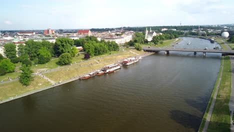 Riverbanks-with-moored-boats,-green-parks,-pathways,-and-historic-buildings-in-Krakow,-Poland