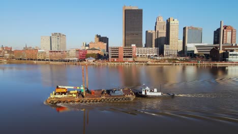 Barge-steaming-down-the-Maumee-River,-in-downtown-Toledo-with-ProMedica-Headquarters-in-the-background