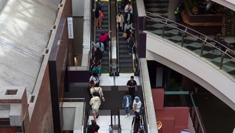 People-taking-the-escalators-up-and-down-during-rush-hours-at-Melbourne-Central-Station,-a-shopping-and-commercial-precinct-in-downtown-area,-featuring-the-entrance-of-the-Coop's-Shot-Tower-Museum