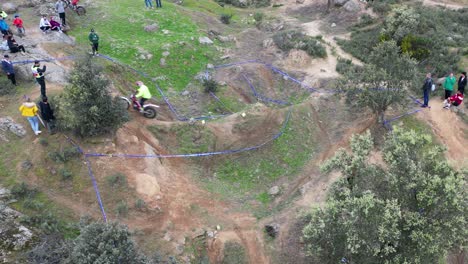 Seitlicher-Flug-Bei-Einem-Outdoor-Motocross-Tageswettbewerb,-Bei-Dem-Der-Pilot-Auf-Der-Mit-Blauem-Band-Markierten-Strecke-In-Aktion-Ist,-Die-Richter-Der-Organisation-Und-Zahlreiche-Zuschauer-Sind-Anwesend