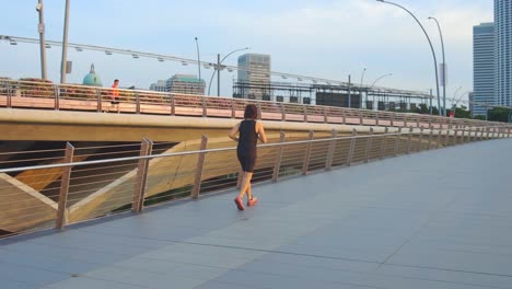 Young-Woman-With-Bob-Haircut-Running-Across-Bridge-Near-City-Park