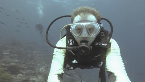 A-diver-takes-a-selfie-against-deep-blue-water-and-second-diver-in-Raja-Ampat,-Indonesia