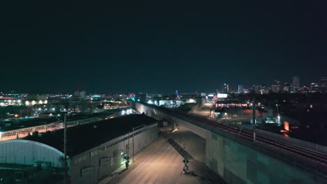 Commuter-rail-crosses-along-bridge-at-night-with-Denver-city-skyline-in-distance