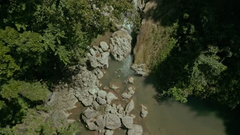 Rocks-in-water-and-trees-next-to-waterfall-in-Philippines,-aerial-rise