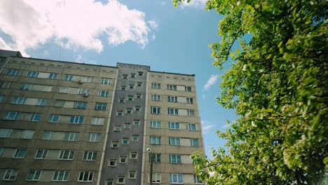 The-footage-pans-from-a-lush-green-tree-to-a-high-rise-grey-residential-apartment-building,-capturing-the-contrast-between-nature-and-urban-living