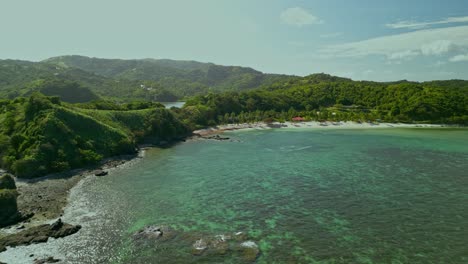 Turquoise-water-by-green-hilly-landscape,-Philippines,-wide-aerial-pan