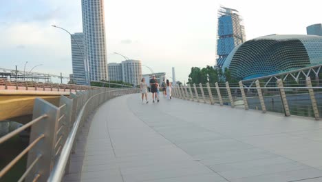 Female-And-Male-Do-Morning-Jogging-On-Modern-Pedestrian-Bridge-Near-City-Buildings