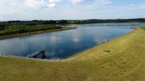 Aerial-view-lowering-to-water-supply-reservoir-blue-sky-reflections-in-rural-countryside-lake