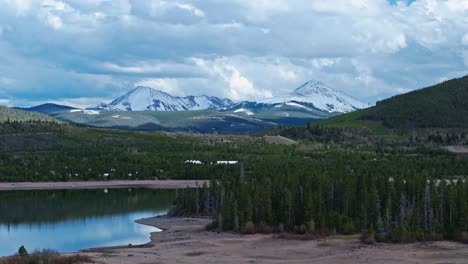 Aerial-Pan-Etabliert-Immergrüne-Pflanzen-Rund-Um-Dillon-Reservoir-In-Frisco-Colorado-Mit-Schneebedeckten-Bergen