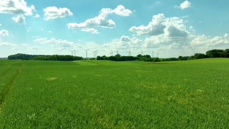 Vista-Aérea-De-Vastos-Campos-Verdes-Con-Turbinas-Eólicas-Y-Un-Cielo-Azul-Brillante-Con-Nubes-Esponjosas