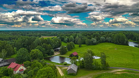 Rural-cottage-by-a-lake,-fields-and-trees---cloudscape-aerial-hyper-lapse