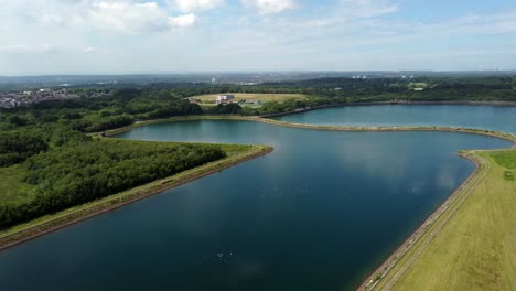 Vista-Aérea-Descendiendo-Al-Depósito-De-Suministro-De-Agua-Reflejos-Del-Cielo-Azul-En-El-Lago-Rural