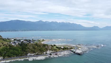 Drone-view-of-Kaikoura,-the-ocean-and-mountains-behind-in-New-Zealand