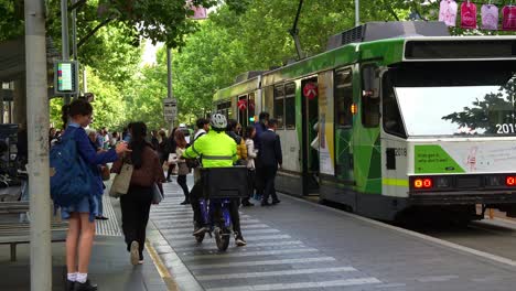 Passengers-disembarking-and-boarding-the-tram-at-the-stop-on-Swanston-street,-in-the-bustling-Melbourne-central-business-district,-cyclists-cycling-through-the-lane,-a-vibrant-urban-lifestyle