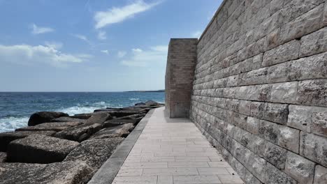 Walking-Along-the-Fortified-Walls-of-Monopoli-with-Waves-Hitting-the-Shoreline,-Bari,-Italy