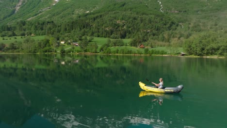 Kayaker-paddling-on-a-serene-lake-surrounded-by-lush-green-mountains-and-clear-skies-in-Olden,-Norway