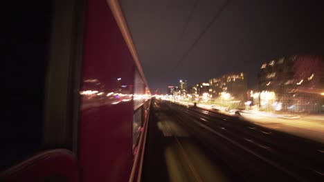 Fast-Train-speeding-at-night,-exterior-window-view,-fast-lights-from-cars-and-buildings-passing-quickly-angle-and-shot-with-the-city-in-the-background-outside-external-perspective-Outdoor,-motion-blur