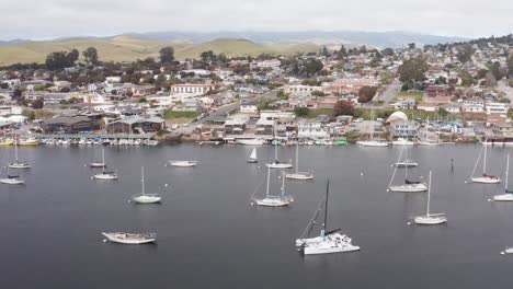 Low-aerial-dolly-shot-of-the-Morro-Bay-Embarcadero-with-sailboats-in-the-harbor-in-Morro-Bay,-California