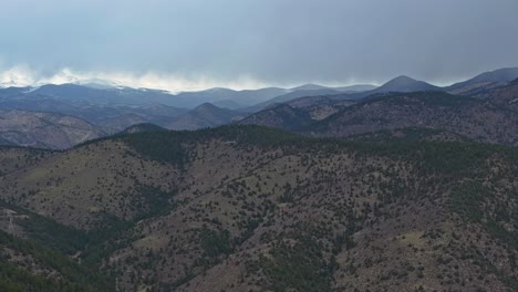 Evergreen-trees-cover-sloping-hillside-of-rocky-mountains-under-overcast-stormy-sky-in-Colorado