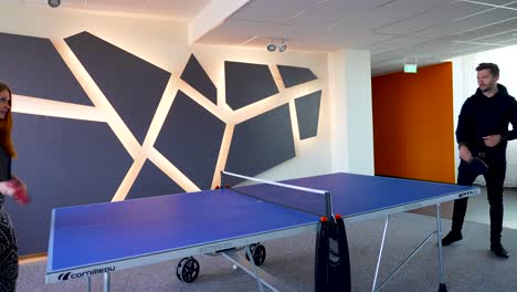 A-man-and-a-woman-playing-ping-pong-with-rackets-in-an-office-during-the-daytime,-on-a-beautiful-ping-ping-table-and-orange-ball