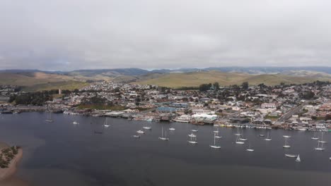 Aerial-low-panning-shot-of-sailboats-lined-up-in-the-harbor-along-the-Embarcadero-in-Morro-Bay,-California