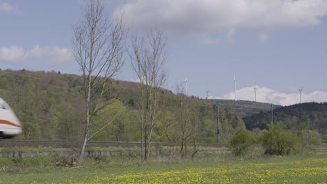 High-speed-train-speeding-through-a-scenic-landscape-with-wind-turbines-on-a-sunny-day,-blurred-motion