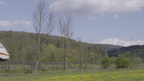 Hochgeschwindigkeitszug-Rast-An-Einem-Sonnigen-Tag-Durch-Eine-Malerische-Landschaft-Mit-Windturbinen,-Bewegungsunschärfe