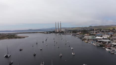 Low-aerial-shot-flying-over-sailboats-in-the-harbor-towards-the-Morro-Bay-Power-Plant-in-Morro-Bay,-California
