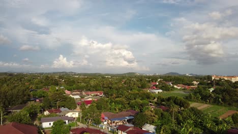 Slow-flying-straight-on-with-palm-trees-and-village-kampung-houses-with-creamy-white-and-blue-skies-during-mid-afternoon-in-Melaka-Malaysia