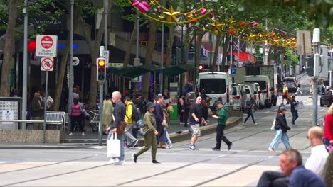 Pedestrians-cross-the-street-on-Bourke-Street-in-the-vibrant-Melbourne-Central-Business-District,-where-the-street-is-adorned-with-festive-decorations