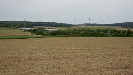 Hochgeschwindigkeitszug-Rast-Durch-Ländliche-Landschaft-Mit-Feldern-Und-Windturbinen