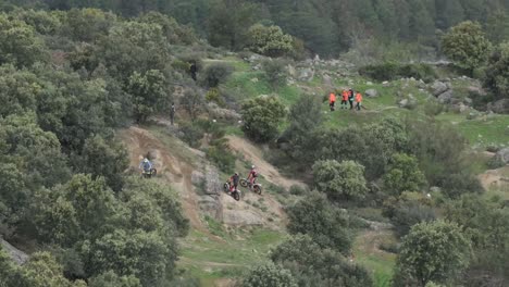 Flug-Zur-Beobachtung-Der-Vorbereitungen-Für-Eine-Motocross-Meisterschaft-Auf-Dem-Feld,-Wo-Teilnehmer-Mit-Motorrädern-Und-In-Orange-Gekleidete-Mitglieder-Des-Zivilschutzes-Auf-Dem-Weg-Zu-Ihren-Positionen-Erscheinen