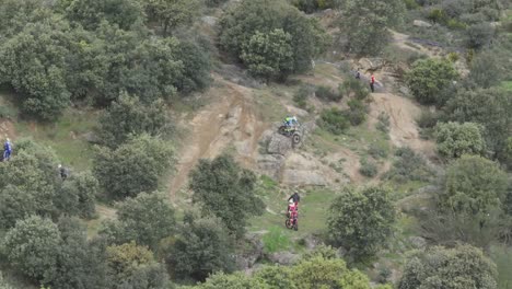Drone-flight-observing-the-preparation-of-a-motocross-championship-where-there-are-contestants-with-motorcycles-going-up-and-down-a-dirt-embankment-to-prepare,-there-are-observers