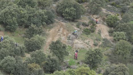 Vuelo-De-Drone-Observando-La-Preparación-De-Un-Campeonato-De-Motocross-Donde-Hay-Concursantes-Con-Motos-Subiendo-Y-Bajando-Un-Terraplén-De-Tierra-Para-Prepararse,-Hay-Observadores