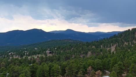 Aerial-pan-above-evergreen-forest-background-under-storm-clouds-above-rocky-mountain-peaks-in-Colorado