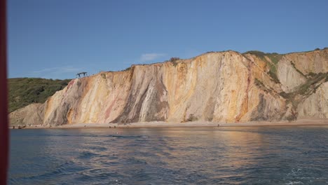 Cliffs-with-vibrant-stratified-colours-by-the-sea,-under-a-clear-blue-sky
