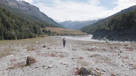 Young-caucasian-woman-walking-through-a-valley-and-river-on-a-sunny-day-with-a-backpack-in-Rees-Dart-track,-New-Zealand