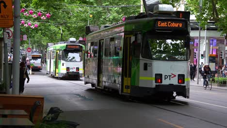 A-busy-urban-street-scene-in-Melbourne,-Australia,-featuring-two-trams-navigating-the-bustling-city-along-Swanston-street,-with-pedestrians-walking-on-the-sidewalks