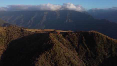 Drone-view-of-a-small-hut-in-between-mountains-during-sunset-at-Mount-Brown,-West-Coast,-New-zealand