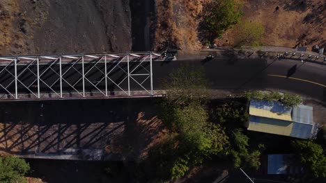 Toma-Aérea-De-Un-Puente-En-Tulamben,-Bali,-Que-Muestra-La-Estructura-Y-El-Paisaje-Circundante-Desde-Arriba-Con-Motocicletas-Circulando-Por-La-Carretera