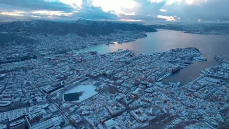 Dense-urban-snow-covered-port-town-of-Bergen-Norway-at-sunset,-aerial-establish