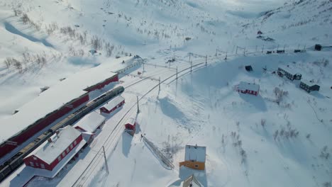 Aerial-of-Myrdal-Train-station-covered-in-snow-in-Norway-at-midday-with-no-people,-wintersports-and-skiing-drone