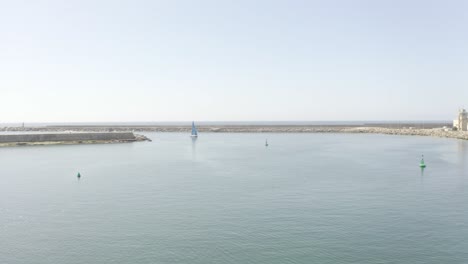 Drone-approaches-and-tilts-as-a-blue-sailboat-enters-docks-from-the-sea