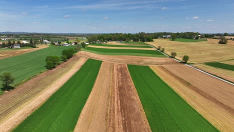 Aerial-lateral-wide-shot-of-agricultural-fields-in-different-colors-during-sunny-day-in-American-countryside