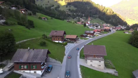 Drone-shot-following-blue-car-driving-in-swiss-mountain-village-in-summer