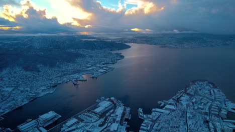 Bergen-drone,-Golden-sunset-glow-spread-across-clouds-above-fjord-Norway-covered-in-snow