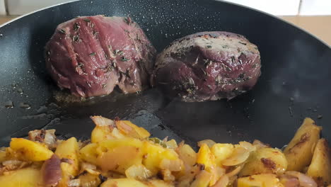 Venison-steaks-seasoned-with-herbs-are-seared-in-a-hot-pan-with-crispy-potatoes