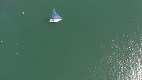 Drone-ascends-and-orbits,-centering-on-a-sailboat-sailing-in-the-sea