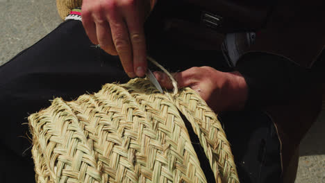 Beautiful-slow-motion-shot-of-an-older-man's-hands-weaving-a-straw-hat-at-a-medieval-fair-in-Andalusia,-Spain